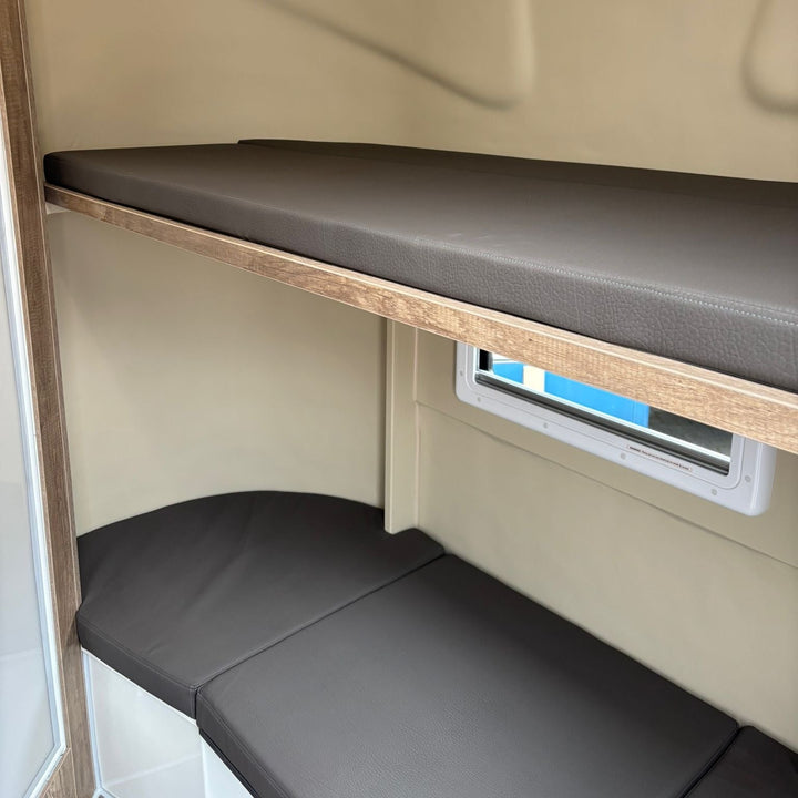 Bunk seating area with grey leather-effect cushions arranged over the wheel arch beneath a side window