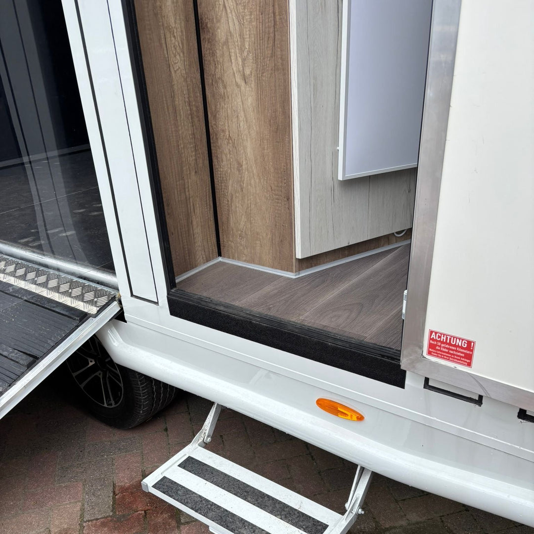 External groom door open with the fold-down step deployed for access into the living area