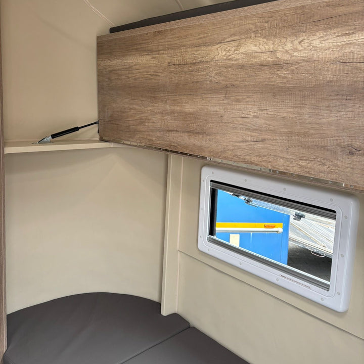 Overcab luton bunk space with wood-effect overhead cabinet and side window
