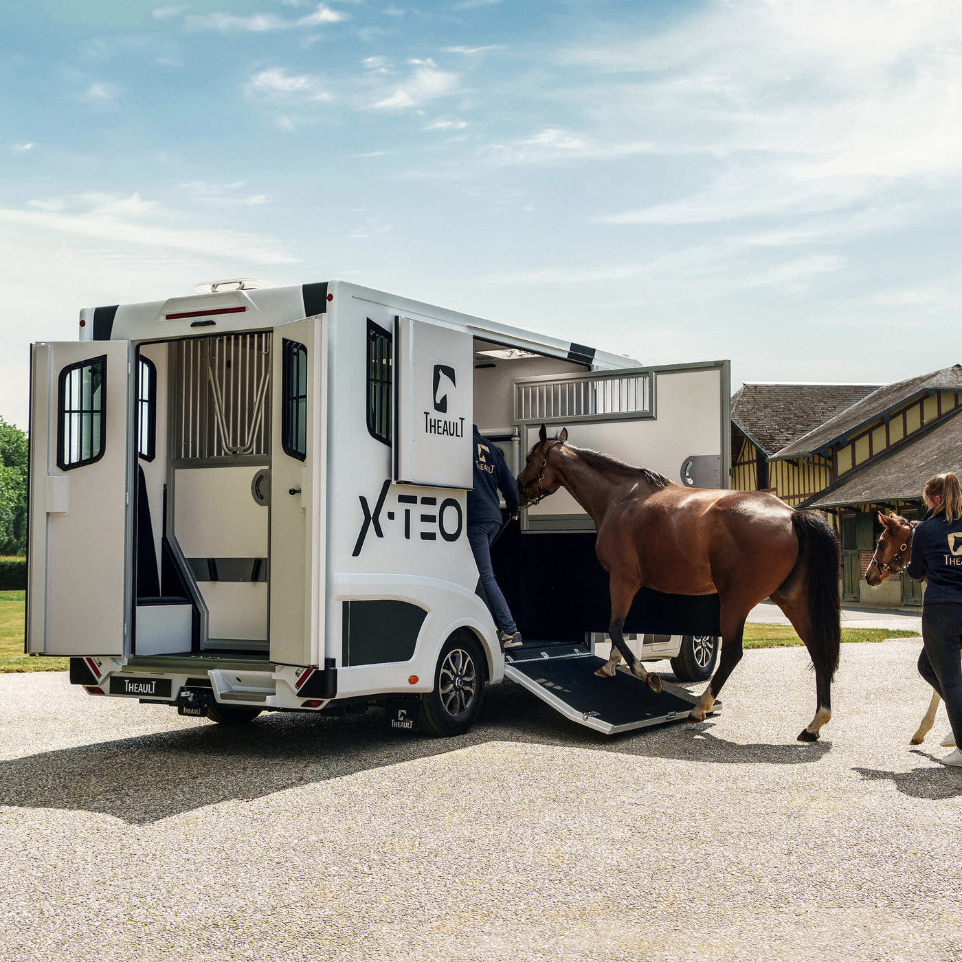 Theault XTEO horsebox with its rear ramp down and two horses being loaded outside a Normandy stable yard