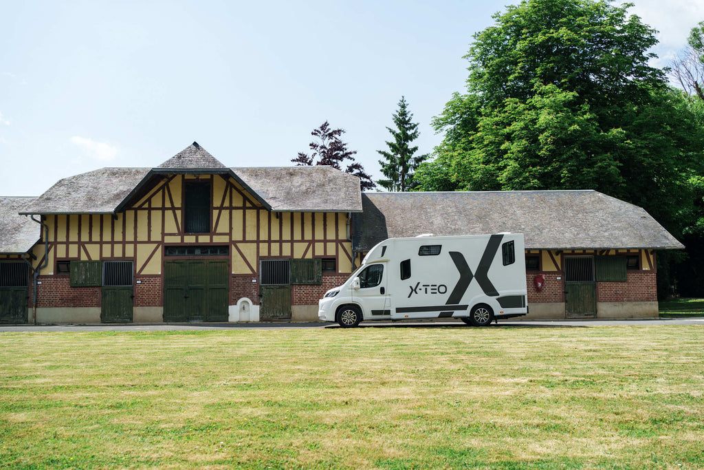 Side view of a Theault XTEO horsebox alongside a long half-timbered Normandy stable building
