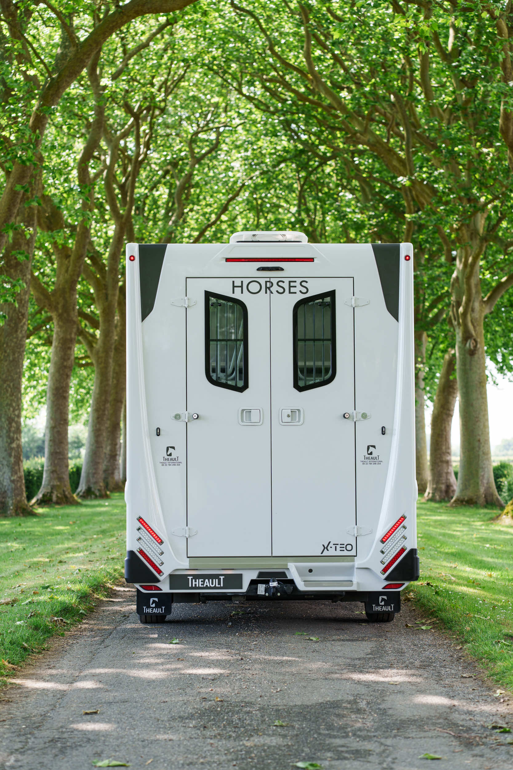 Rear view of a Theault XTEO horsebox with the ramp closed on a tree-lined avenue