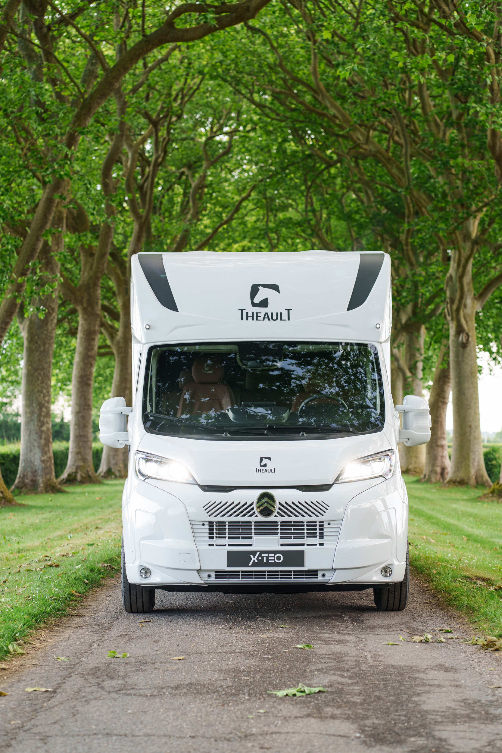 Head-on front view of a Theault XTEO horsebox on a tree-lined avenue